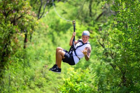 Smiling guest ziplining through green trees at Coral Crater Adventure Park in Kapolei, Oahu
